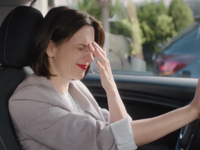  Eine überfordert wirkende Frau sitzt auf dem Fahrersitz im Auto.