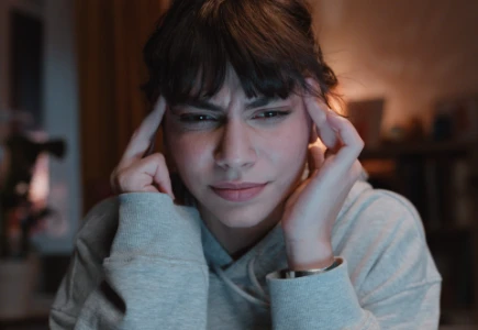  Eine Studentin hält sich die Hände an die Schläfen und hat Kopfschmerzen.