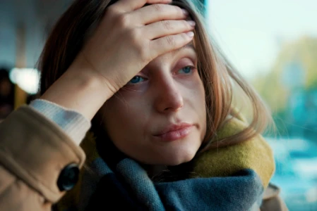  Eine müde aussehende Frau hält ihre Hand auf ihre Stirn.