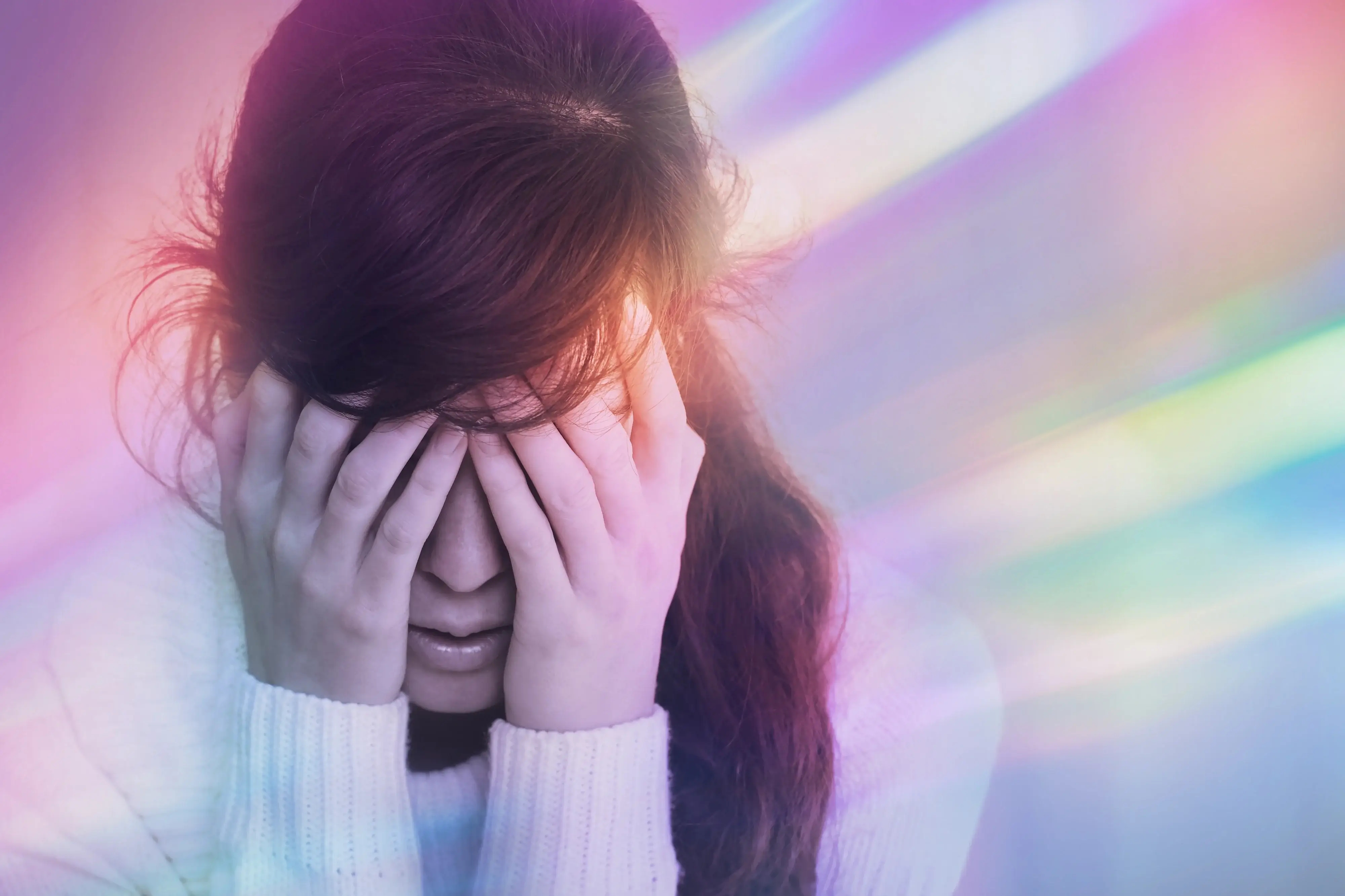 Eine Frau stützt ihren Kopf auf ihre Hände. Der Hintergrund ist bunt, um einen Eindruck von der Aura zu vermitteln.
