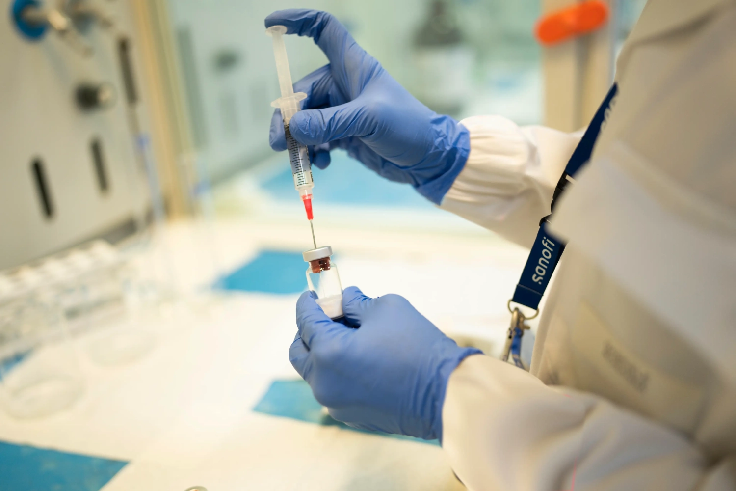 Nahaufnahme von Händen in Handschuhen im Labor, die eine Ampulle und Spritze in der Hand halten