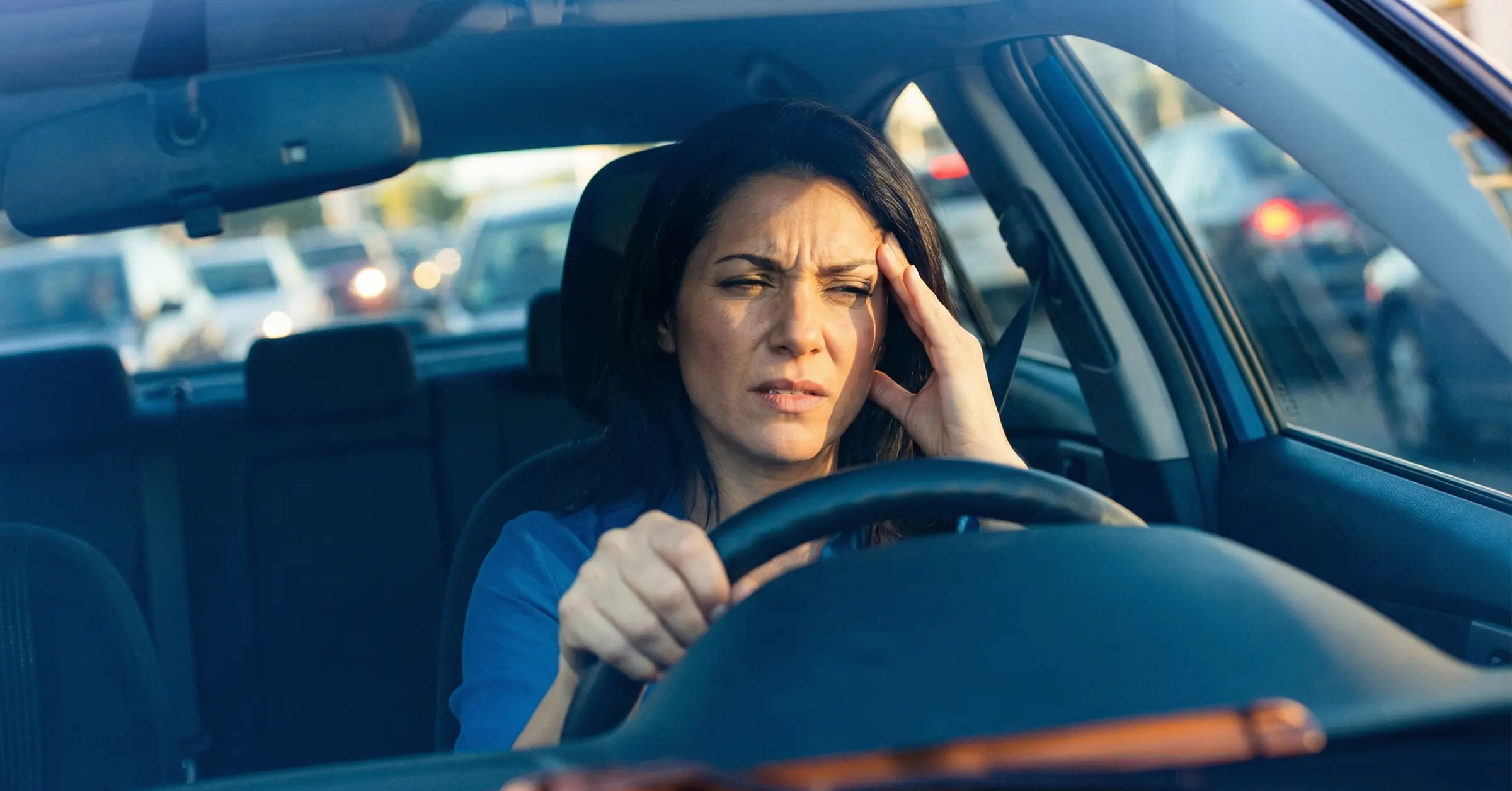  Eine überfordert wirkende Frau sitzt auf dem Fahrersitz im Auto.